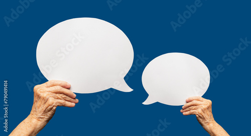 Close-up of a senior woman's hands holding a blank white speech bubble against a blue background.