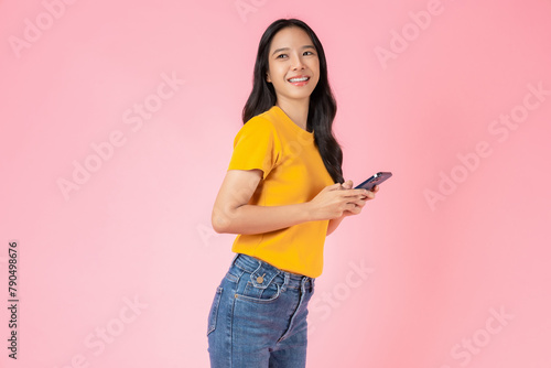 Beautiful Asian woman holding smartphone and smiling on pink background.