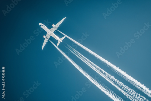A commercial airplane soars through a clear blue sky  leaving a trail of white contrails behind it  high above