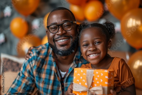 Father and daughter pose with a gift, surrounded by balloons, in a festive atmosphere.