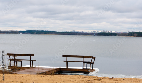 A small pier with a wooden bench on the shore of a winter lake.