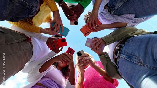 Young group of student women using smartphone together outside. Addicted millennial female friends using cell phone at city street. Low angle view.