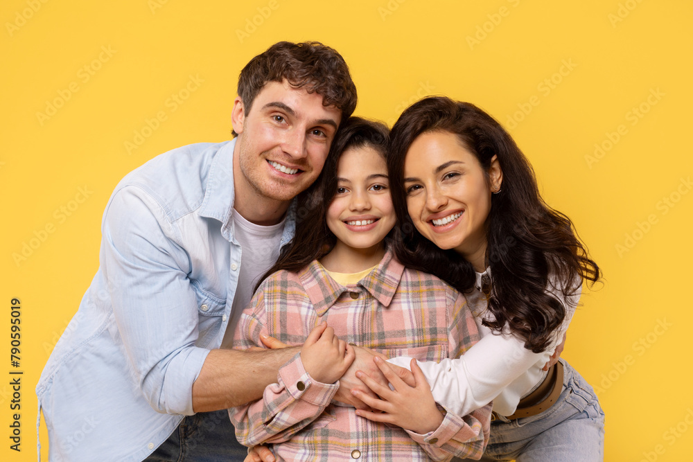 Closeup photo of three family members, mother father and daughter hugging happy together, posing isolated on yellow background Closeup photo of three family members, mother father and daughter hugging happy together, posing isolated on yellow background
