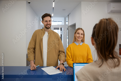 Happy man and woman couple signing document at modern clinic reception desk