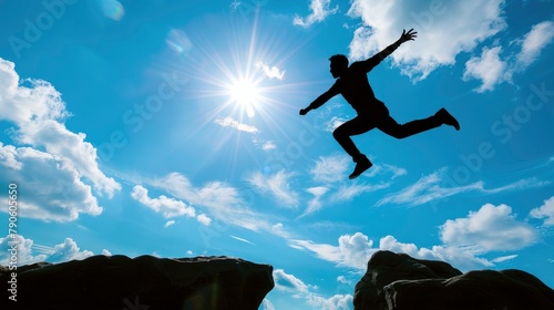 Man leaping across a chasm in silhouette against a backdrop of the blue sky and sun