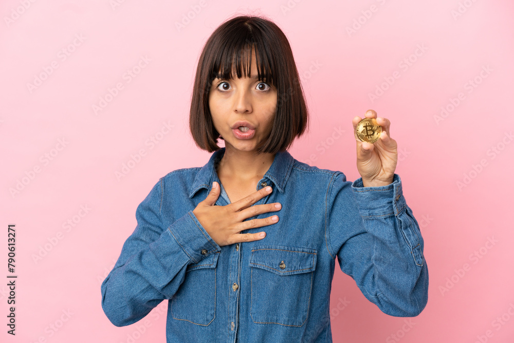 Young mixed race woman holding a Bitcoin isolated background surprised and shocked while looking right Young mixed race woman holding a Bitcoin isolated background surprised and shocked while looking right