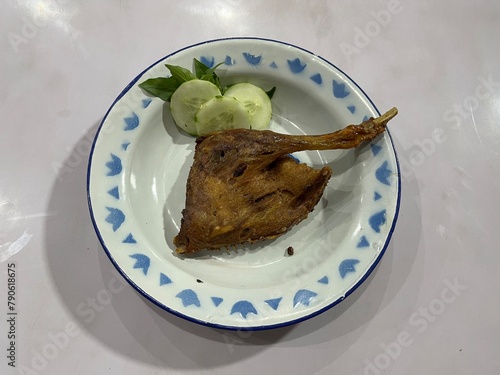 Indonesian traditional deep fried duck thigh and leg served on a plate with slices of cucumber and basil leaves