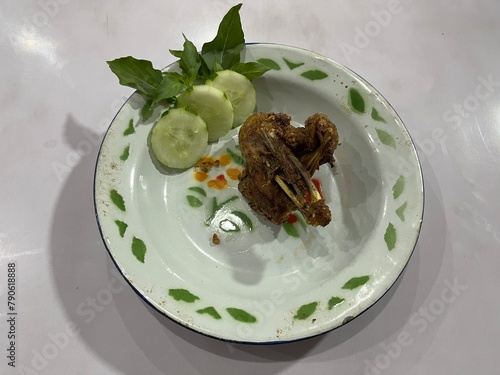 Indonesian traditional deep fried duck breast served on a plate with slices of cucumber and basil leaves