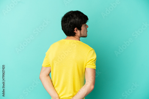 Young Russian man isolated on blue background in back position and looking back