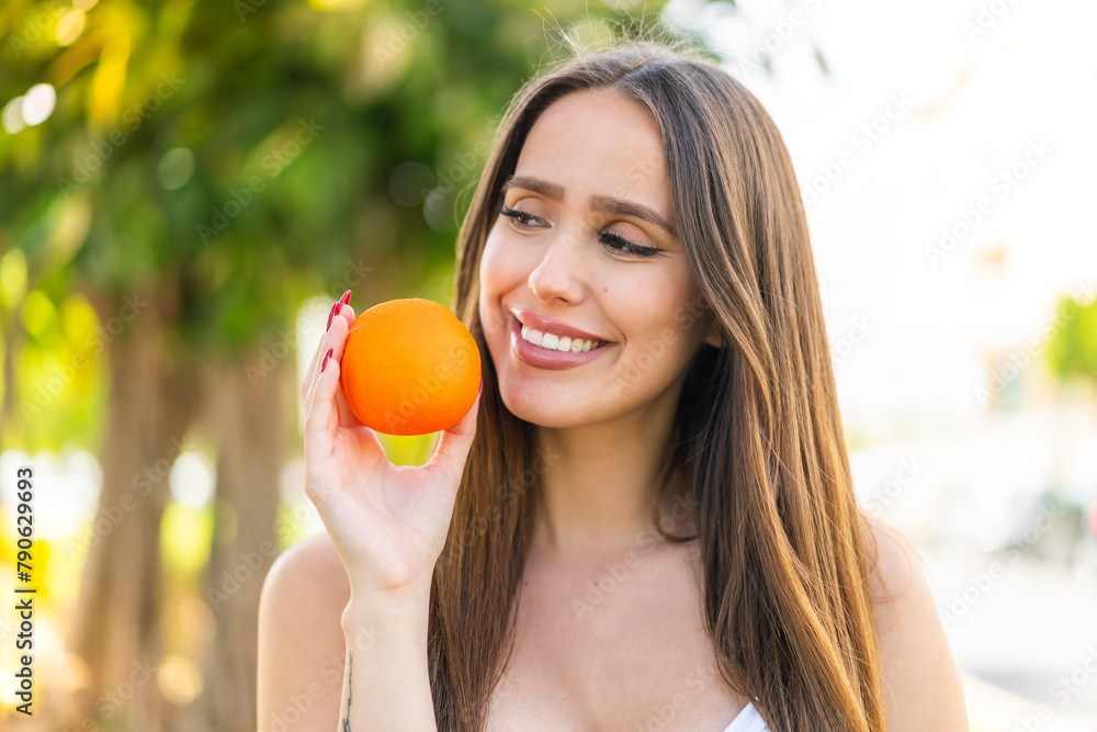 Young woman at outdoors holding an orange with happy expression Young woman at outdoors holding an orange with happy expression