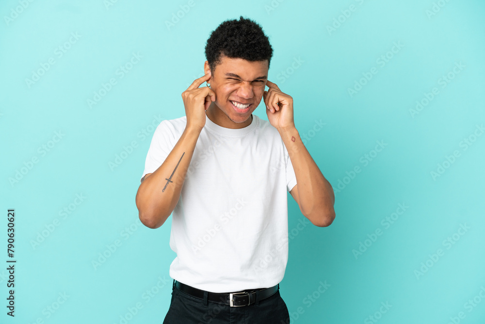 Young African American man isolated on blue background frustrated and covering ears Young African American man isolated on blue background frustrated and covering ears