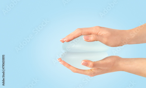 Two breast implants in hands on blue background , copy space.
