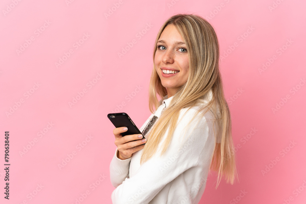 Young blonde woman isolated on pink background holding a mobile phone and with arms crossed Young blonde woman isolated on pink background holding a mobile phone and with arms crossed