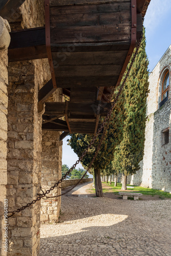 Medieval ingenuity on display with the counterweight system of a drawbridge in Brescia historic castle, framed by a stony arch and flanked by cypress trees
