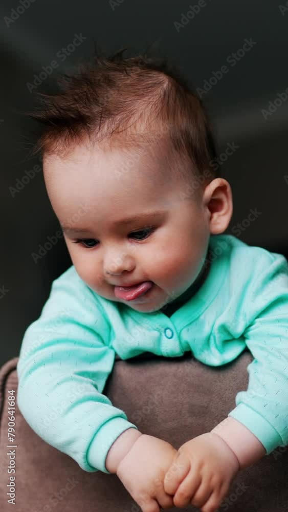 Cute kid standing on chair looking down. Adorable baby showing tongue. Low angle view. Blurred backdrop. Vertical video Cute kid standing on chair looking down. Adorable baby showing tongue. Low angle view. Blurred backdrop. Vertical video