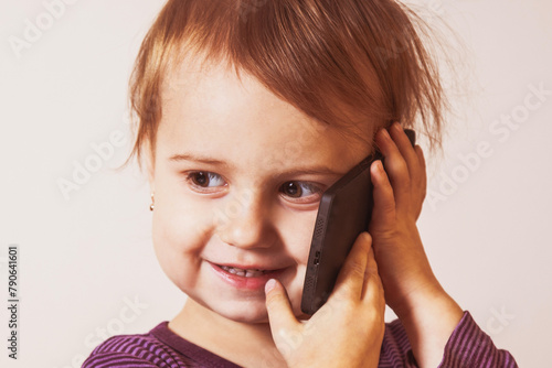 Little smiling beautiful child girl is speaking with smart phone