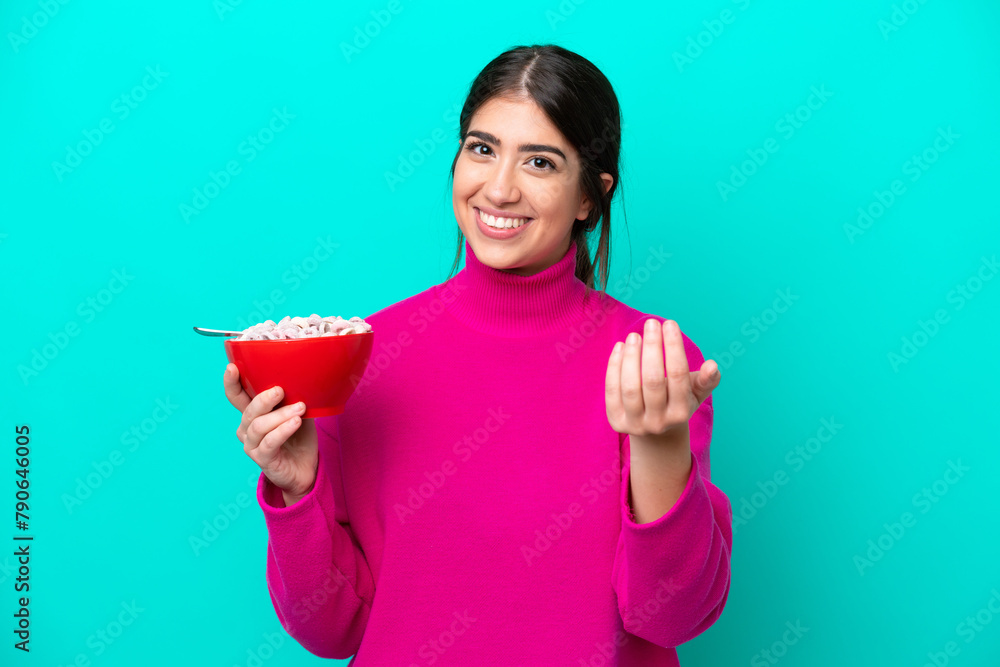 Young caucasian woman holding a bowl of cereals isolated on blue background inviting to come with hand. Happy that you came Young caucasian woman holding a bowl of cereals isolated on blue background inviting to come with hand. Happy that you came