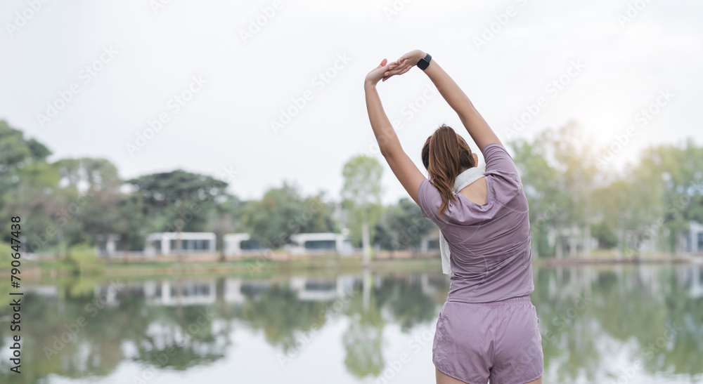 Asian woman is stretching her arms out in front of a lake