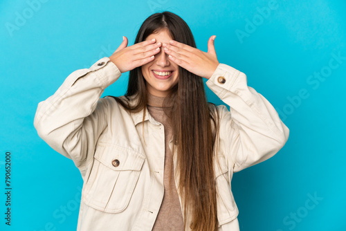 Young caucasian woman isolated on blue background covering eyes by hands and smiling