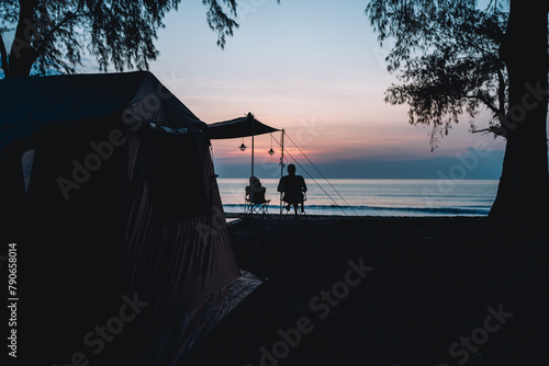 man and a teddy bear sit on a chair having a rest in front of tent at campfire under morning sky, Outdoor lifestyle concept.