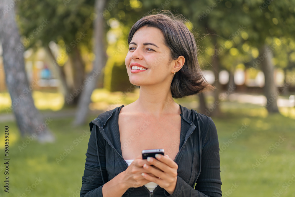 Young pretty Bulgarian woman at outdoors using mobile phone and looking up Young pretty Bulgarian woman at outdoors using mobile phone and looking up