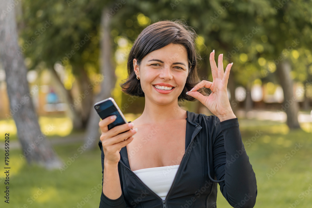 Young pretty Bulgarian woman at outdoors using mobile phone and doing OK sign Young pretty Bulgarian woman at outdoors using mobile phone and doing OK sign