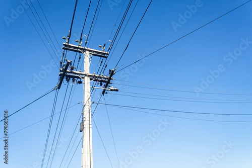 Low angle view of power post and powerlines against a cloudless blue sky. Auckland.