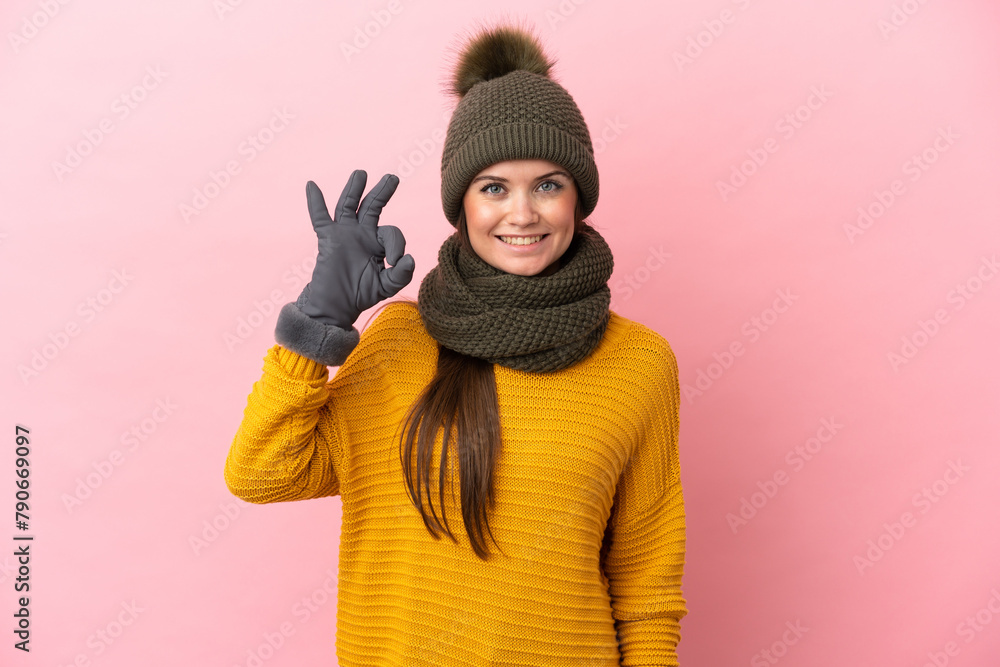 Young caucasian girl with winter hat isolated on pink background showing ok sign with fingers Young caucasian girl with winter hat isolated on pink background showing ok sign with fingers