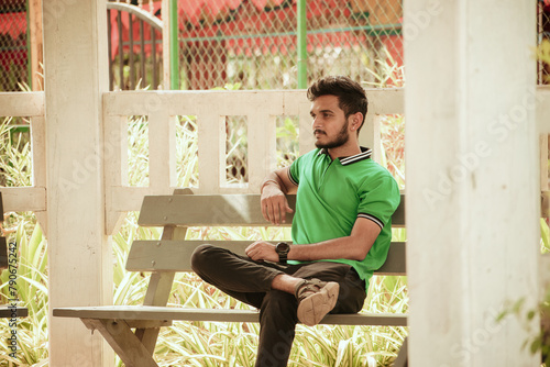 Young handsome Indian man sitting on bench in the park.