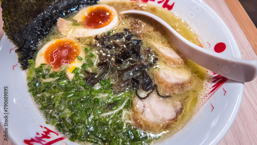 High angle top view photo of Japanese miso ramen consisting of broth, miso, chicken, sliced scallions, sliced mushrooms, soft half boiled egg or ajitsuko tamago ajitama in a bowl on a wooden table.
