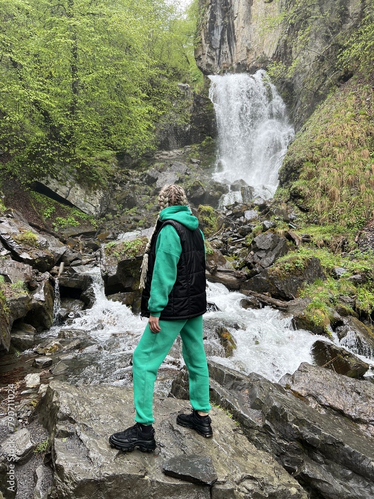 A woman on the background of the Lyazhginsky waterfall in the spring forest. A cascading waterfall surrounded by greenery. Splashes of water. The water flows along the Lyazhgi River. Ingushetia A woman on the background of the Lyazhginsky waterfall in the spring forest. A cascading waterfall surrounded by greenery. Splashes of water. The water flows along the Lyazhgi River. Ingushetia
