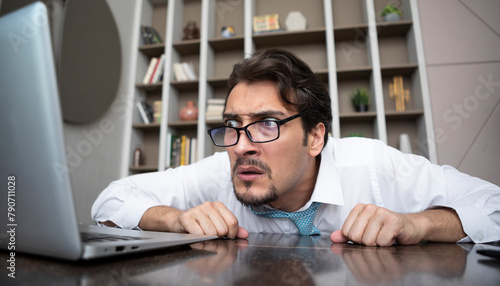Shocked businessman hiding behind desktop and looking at laptop in the office. Business crisis and bankruptcy concept