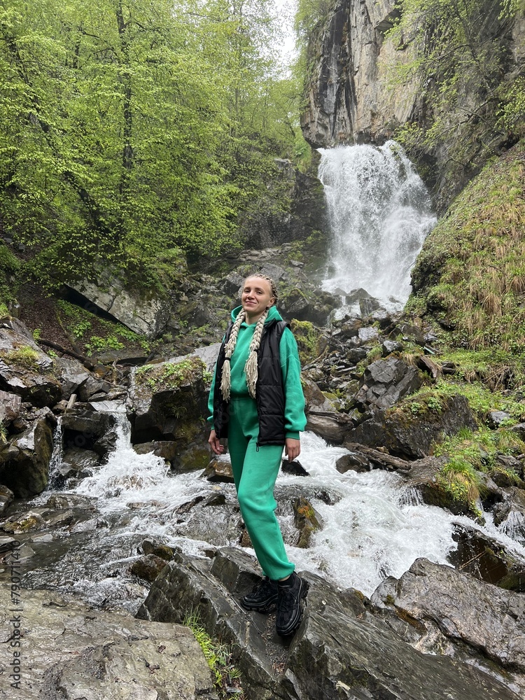 A woman on the background of the Lyazhginsky waterfall in the spring forest. A cascading waterfall surrounded by greenery. Splashes of water. The water flows along the Lyazhgi River. Ingushetia