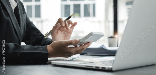 Close up Business woman using calculator and laptop for do math finance on wooden desk in office and business working background, tax, accounting, statistics and analytic research concept