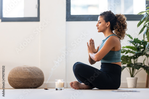 Sporty young woman doing yoga and hypopressive exercises while staying in lotus position in living room at home.