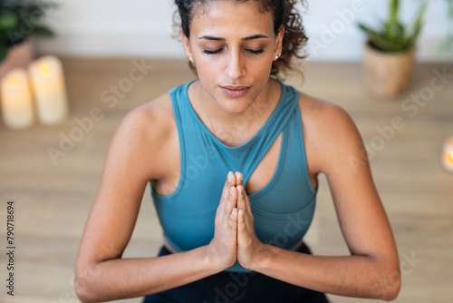 Sporty young woman doing yoga and hypopressive exercises while staying in lotus position in living room at home.