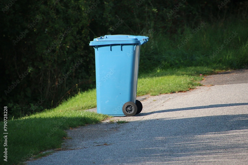 Large blue plastic trash can for waste paper stands alone on the side of the road, waiting to be picked up Large blue plastic trash can for waste paper stands alone on the side of the road, waiting to be picked up