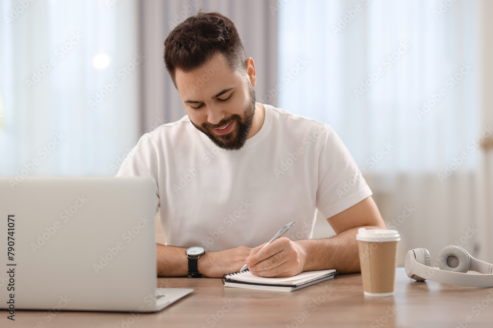 Young man writing down notes during webinar at table in room