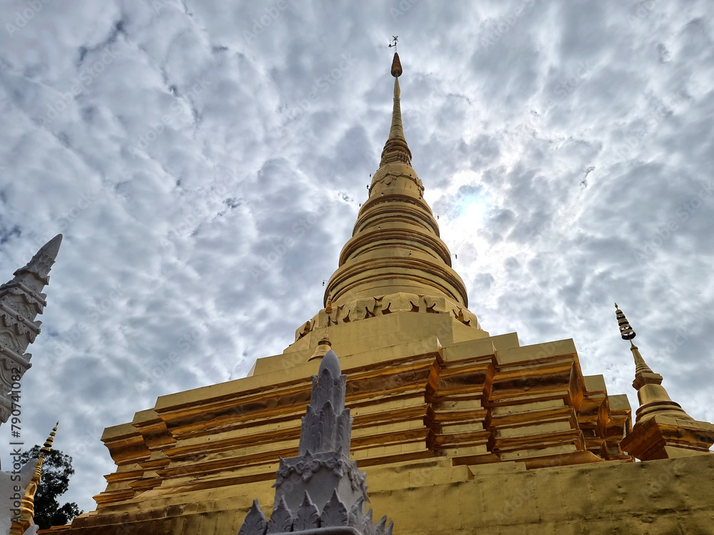 Fototapeta premium The perspective of a beautiful tall gold-colored chedi on clouds in the sky background of Wat Phra That Chae Haeng in Nan Province, Thailand.