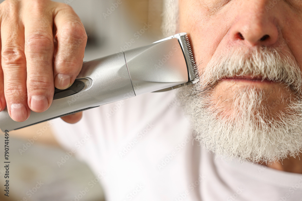 Man trimming beard with electric trimmer indoors, closeup - obrazy, fototapety, plakaty 