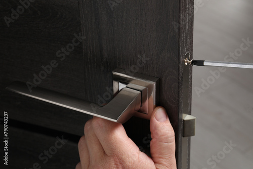 Handyman with screwdriver repairing door handle indoors, closeup photo