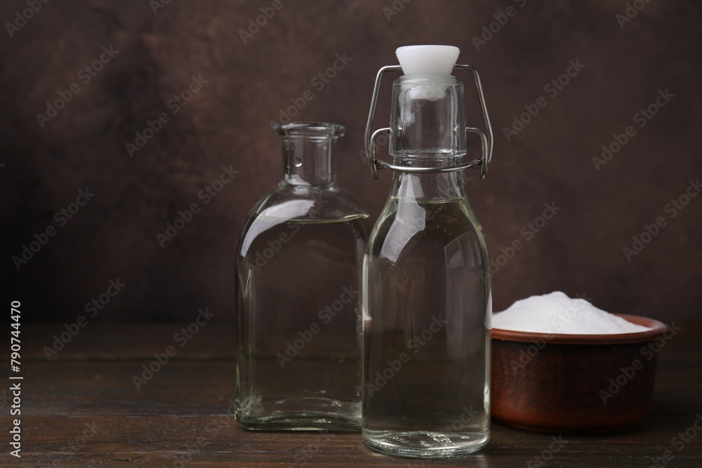 Vinegar in glass bottles and baking soda on wooden table, space for text