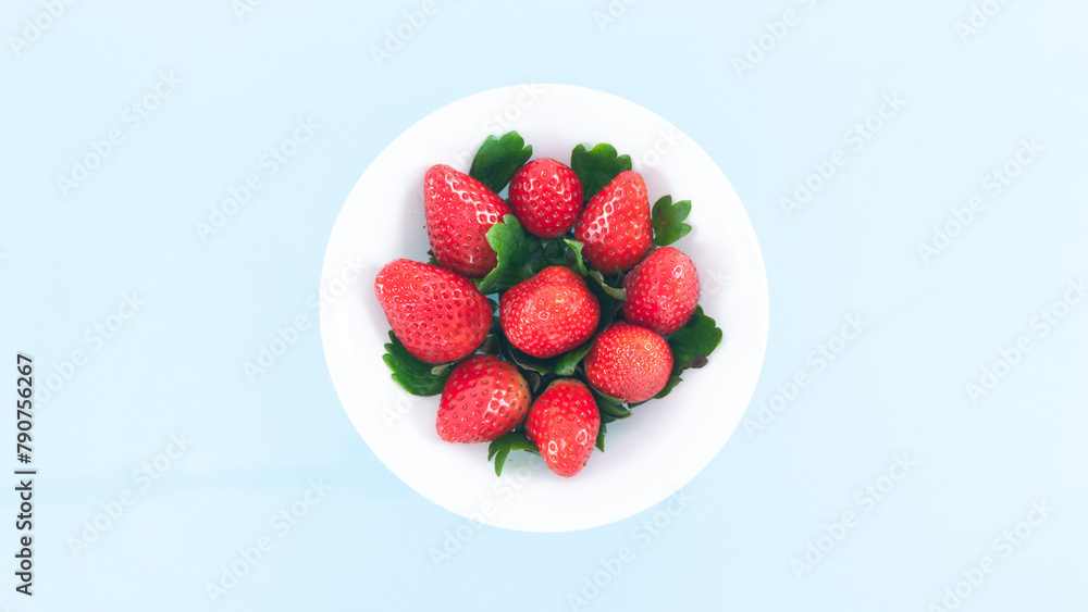 White plate is filled with beautiful juicy red strawberries with beautiful green leaves. Summer concept. White plate is filled with beautiful juicy red strawberries with beautiful green leaves. Summer concept.