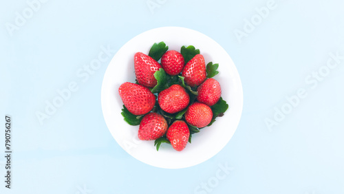 White plate is filled with beautiful juicy red strawberries with beautiful green leaves. Summer concept.