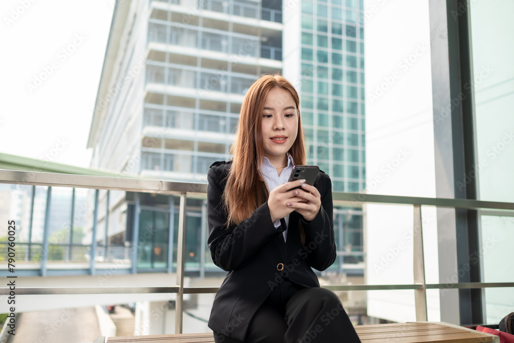 Happy young Asian female businesswoman using cell phone smartphone and holding document files phone at the walkway Happy young Asian female businesswoman using cell phone smartphone and holding document files phone at the walkway