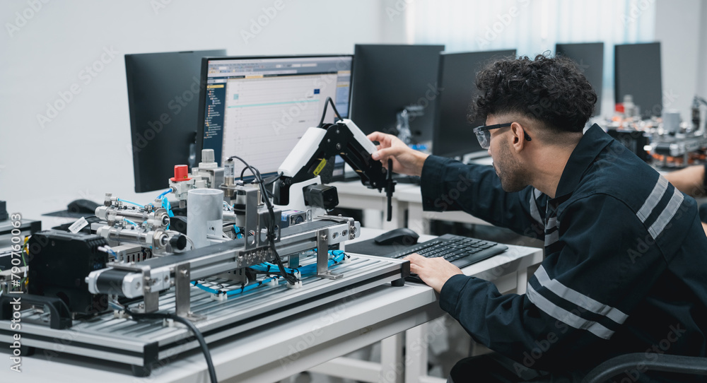 Engineering student assembling a robotic arm using a computer in a technology workshop. Service engineer holding a robot controller and inspecting the robotic arm's welding hardware. Engineering student assembling a robotic arm using a computer in a technology workshop. Service engineer holding a robot controller and inspecting the robotic arm's welding hardware.