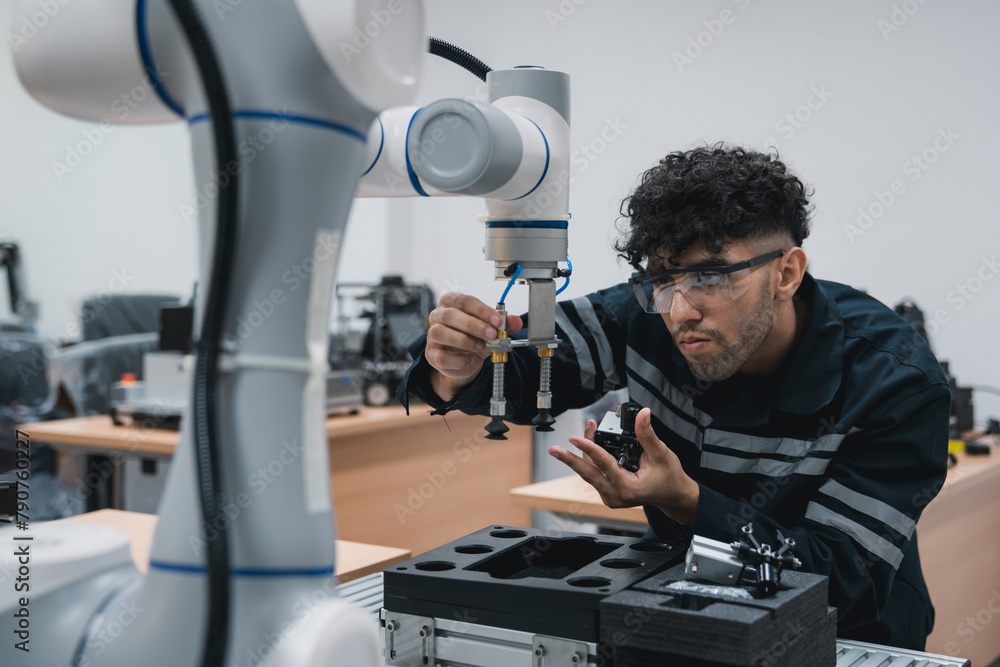 Engineering student assembling a robotic arm using a computer in a technology workshop. Service engineer holding a robot controller and inspecting the robotic arm's welding hardware. Engineering student assembling a robotic arm using a computer in a technology workshop. Service engineer holding a robot controller and inspecting the robotic arm's welding hardware.