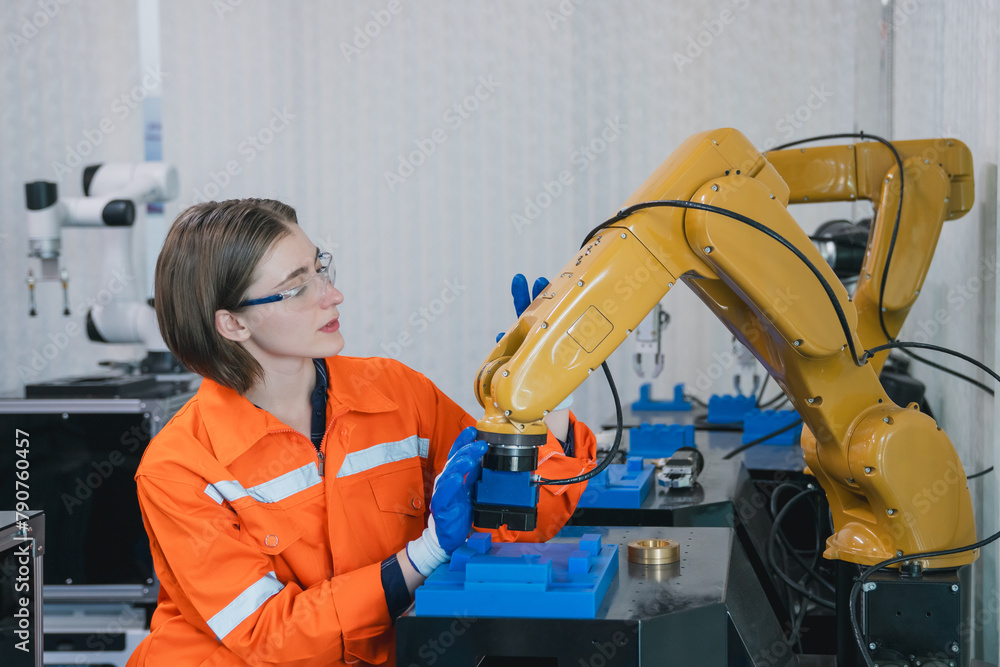 Fototapeta premium Engineering student assembling a robotic arm using a computer in a technology workshop. Service engineer holding a robot controller and inspecting the robotic arm's welding hardware.