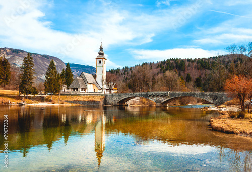 Quaint white chapel and stone bridge over a peaceful river in Slovenia.