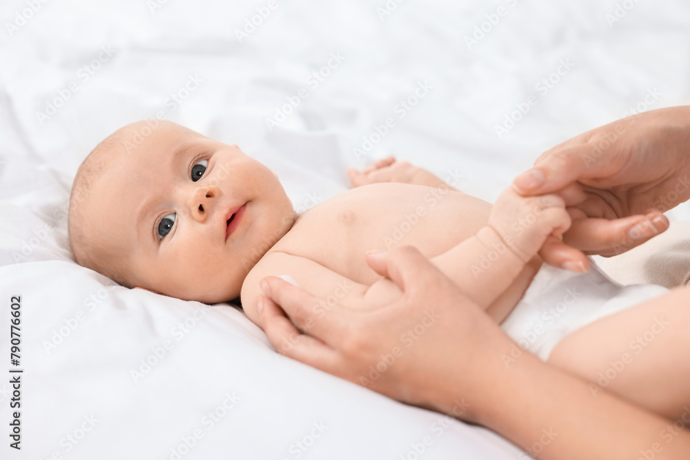 Woman applying body cream onto baby`s skin on bed, closeup Woman applying body cream onto baby`s skin on bed, closeup